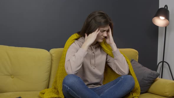 Sick Girl Sits on Sofa Wrapped in Plaid Suffering From Headache or Migraine