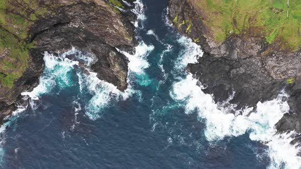 Aerial View of Waves Break on Rocks of Faroe Islands Cliffs in a Blue Ocean alt