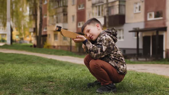 The Boy in Camouflage with Wooden Gun Squats and Aims Forward