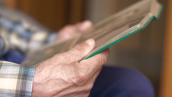 Close-up of the hand of an elderly man holding a family photo album with old black and white photos. alt