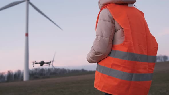 Female Engineer Uses a Drone to Check a System Performance of Wild Turbine or Windmill at Sunset alt