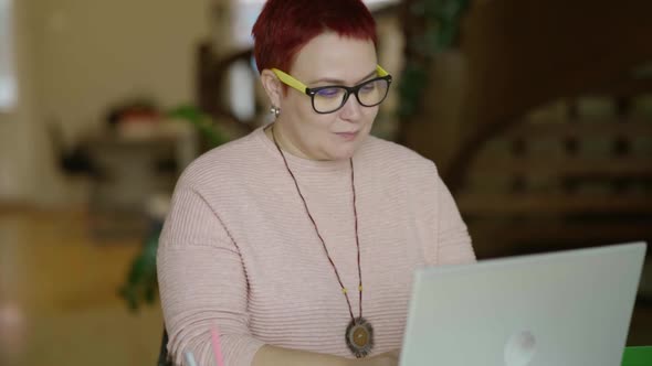 Modern Middleaged Woman in Home Office at Laptop Typing Text Smiling Nonbinary