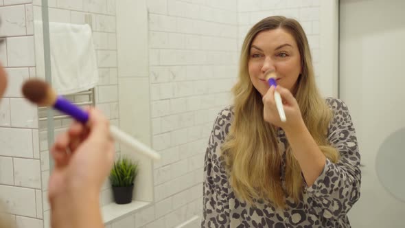 Beautiful Woman Paints Herself with a Brush in the Morning in the Bathroom in Front of the Mirror alt