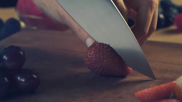 A chef knife used by a woman slices through a strawberry on a kitchen counter