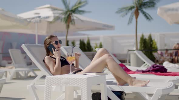 Women Talking on the Phone with Brunette Hair in Black Bikinis Relaxing at a Luxury Resort on a alt