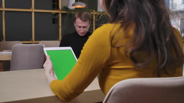 Shooting Over Shoulder of Slim Young Caucasian Woman Sitting in Restaurant Using Tablet with Green alt