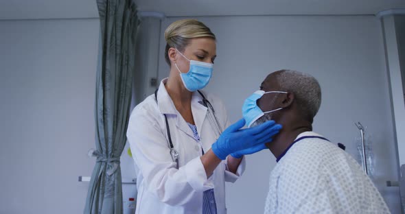Caucasian female doctor wearing face mask examining throat of african american senior male patient alt