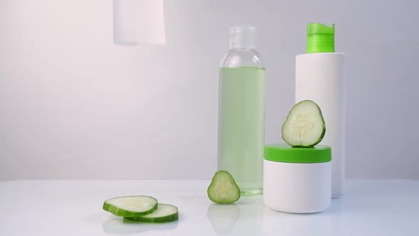 Woman's Hand Take Put Cosmetic White Plastic Bottles with Slices of Fresh Green Cucumber on a White