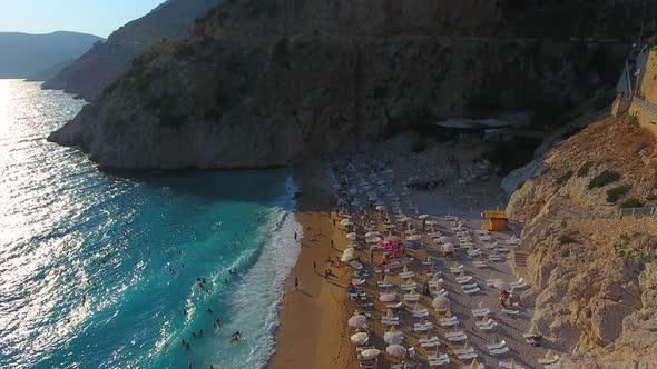 People Swim on Light Blue Sea in the White Sandy Beach Near the Rocky Mountainside alt