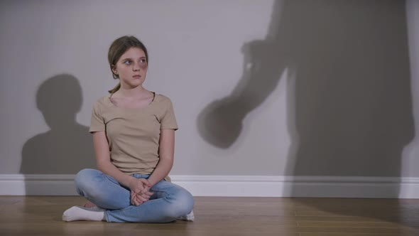 Wide Shot Scared Teenage Caucasian Girl with Bruised Face Sitting on Floor at Wall with Parent alt