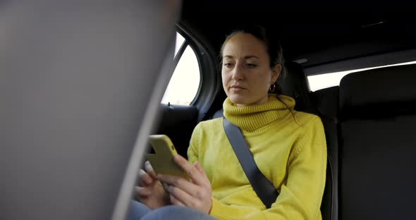 Woman sitting on taxi car back seat, using the phone and looking out of the w