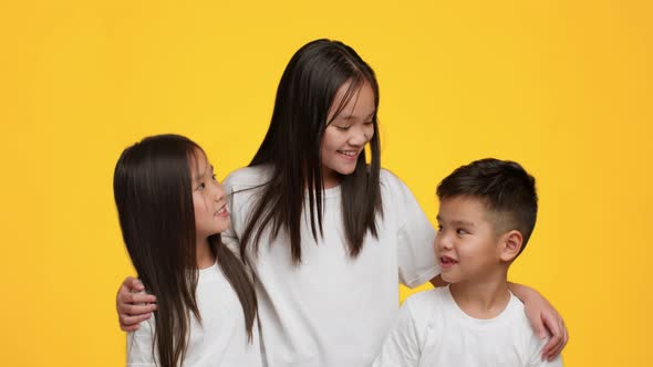 Three Cheerful Korean Siblings Hugging Posing Together Over Yellow Background alt