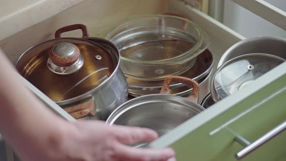 Man hand opening kitchen cupboard door and taking pot by shelf inside alt