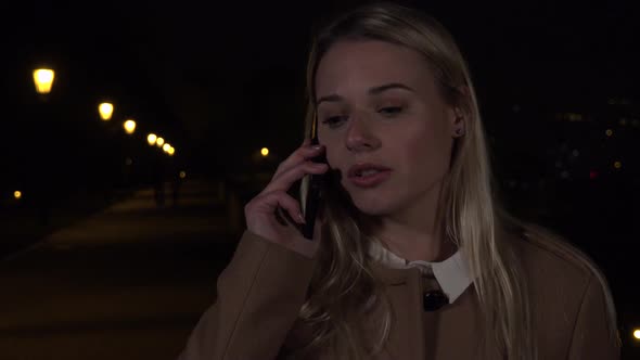 A Young Beautiful Woman Talks on a Smartphone in an Urban Area at Night alt