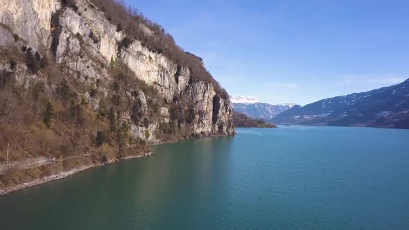 Drone flies straight to a cliff, looking like a fjord. Some birds are flying through the video. alt