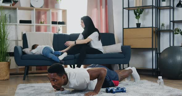 Black-Skinned Man Doing Sport Exercises on Push-Up while His Adorable Smiling Loving Muslim Wife alt