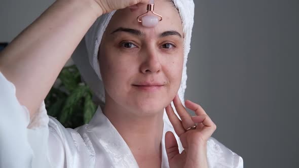 A Closeup Photo of a Young Woman Looking Relaxed and Smiling Doing a Massage with a Face Roller Made