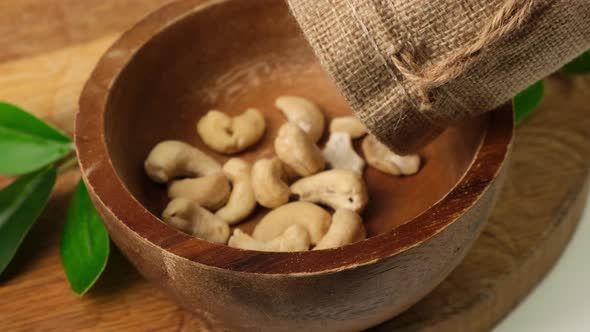 Slow motion dry cashew falling into wooden bowl on board. Close up.