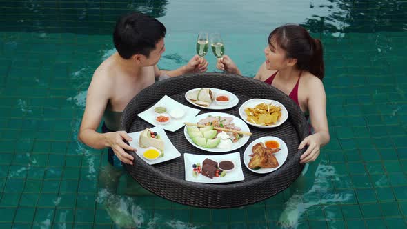happy young couple enjoying with floating food and drinking champagne glass in swimming pool