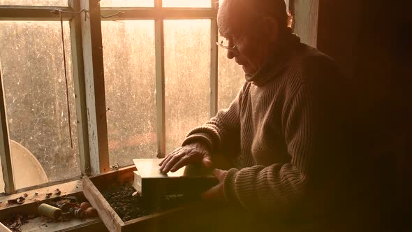 Elderly Man in Glasses Holding Brushing Dust Off Cover Old Book House Window alt