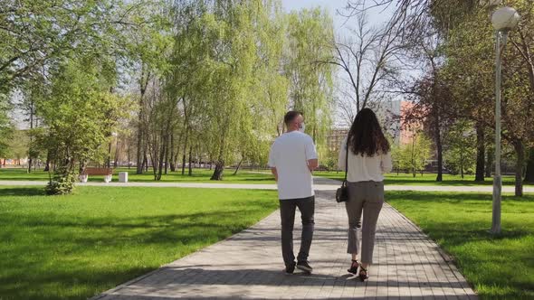 Man and Woman in Face Masks Walking through Park alt
