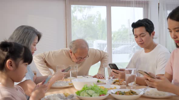 Asian addicted family use mobile phone while eating breakfast on table make grandfather feel upset . alt