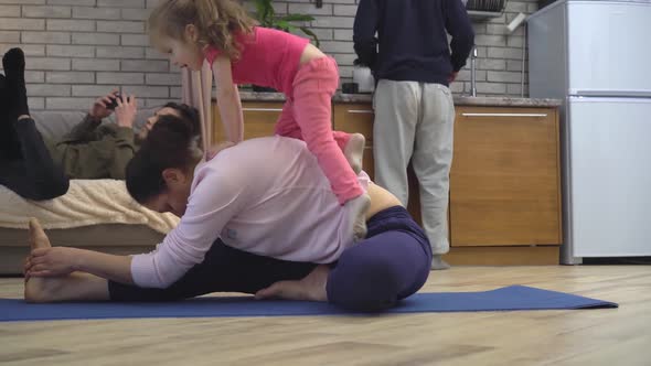 A Mother Tries to Do Yoga at Home in the Kitchen with Her Baby Daughter alt