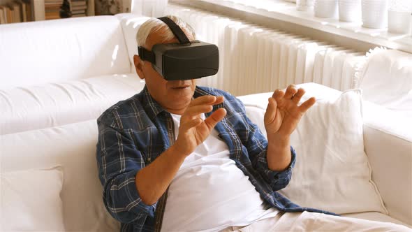 Senior man using virtual reality headset in living room alt