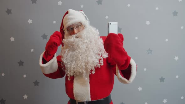 Guy in Santa Costume Dancing Wearing Headphones and Using Smartphone alt