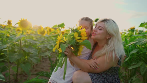 Mother and daughter sing in bouquet flowers on sunflowers field. Females girls have fun outdoors alt