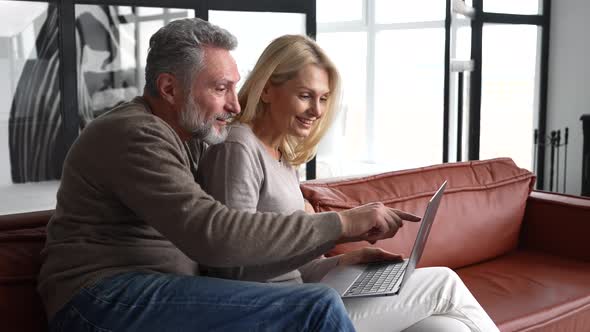 Middleaged Couple Spends Leisure Time with a Laptop at Home alt