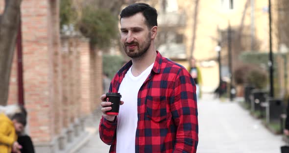 Man holding cup of take-out coffee and smiling standing on street.