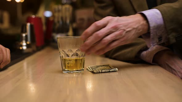 A bar visitor pays for the drink in cash. Close-up of exchanging whiskey for dollars alt