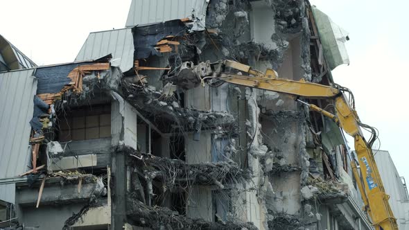 Excavator Destroys the Old Building. Demolition Work, Pieces of Concrete and Reinforcement Fall Down alt
