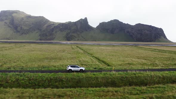 Aerial of Car Driving on a Dirt Road Along Green Fields and Mountains Iceland alt