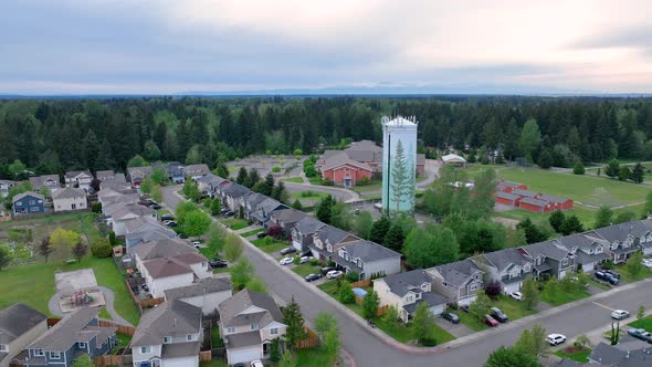 Orbiting aerial shot around a suburban water tower with a neighborhood in the foreground. alt