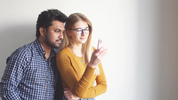 Romantic Multiethnic Couple Choosing Seaside Resort for Their Honeymoon Using Smartphone alt