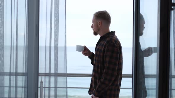 man drinking coffee on the balcony overlooking the sea