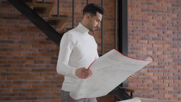 Talented Handsome Middle Eastern Architect Examining Blueprint Standing in Home Office alt
