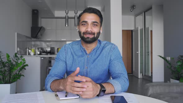 Confident Smiling Indian Man in Earphones Making Video Conference Call alt