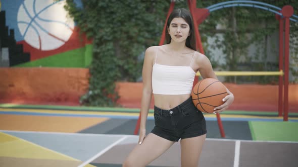 Charming Brunette Sportswoman Posing with Orange Basketball Ball on Outdoor Court alt