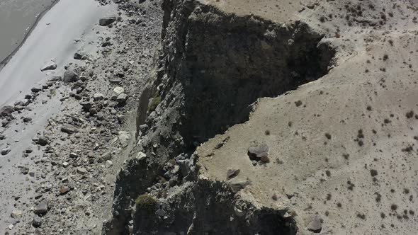 aerial drone flying over a steep mountain cliff overlooking a drop onto the rocks below alt