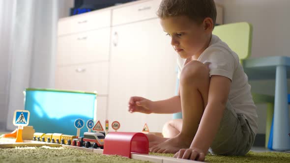 Five Years Old Boy Plays with Wooden Railroad in a Sunny Room