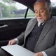 4K Senior businessman sitting on car backseat and working business project on laptop computer