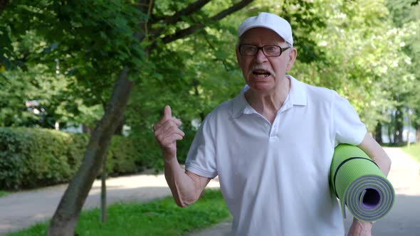 The old grandfather speaks angrily to the camera waving his index finger. alt