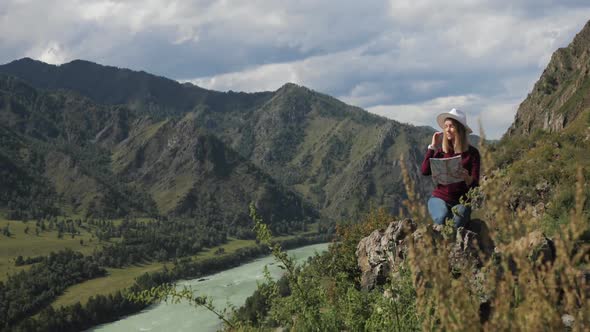 Woman Hiker Sitting on Top of Rocky Mountains Learning Route on Map in Valley alt