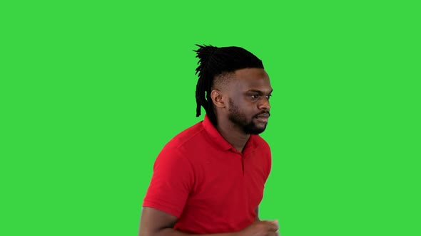 Young African American Man in Casual Clothes Runs and Takes a Look at His Watch on a Green Screen