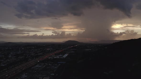 Aerial shot of a highway leading to a hill with heavy clouds on the horizon alt