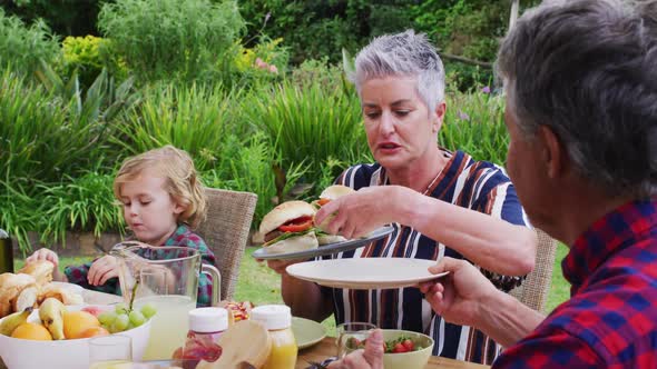 Smiling caucasian senior woman serving family having celebration meal together in garden alt