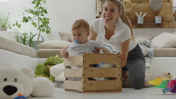 Happy and smiling mom playing with the beautiful baby child inside a wooden box